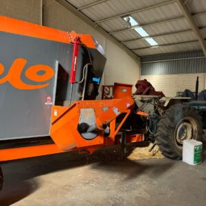 Rolo 8 cube feed mixer connected to a Ford tractor inside a storage shed, showing hydraulic discharge system and auger