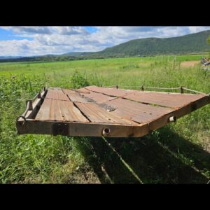 Used 6m Bale Trailer for transporting round and square hay bales or irrigation pipes, shown on grassy farmland with mountain background